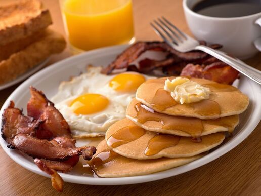 Breakfast plate featuring pancakes, bacon, sunnyside-up eggs, toast, coffee and orange juice