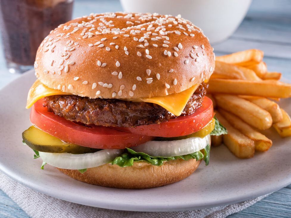 Hamburger topped with cheese, tomato, onion, pickle and lettuce with a side of french fries